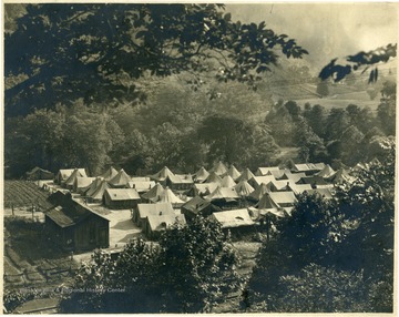 Tent Colony with one house near railroad tracks in valley surrounded by trees.
