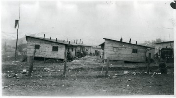 Side view of barracks at Rivesville, W. Va. with car on right and people in distance between barracks.