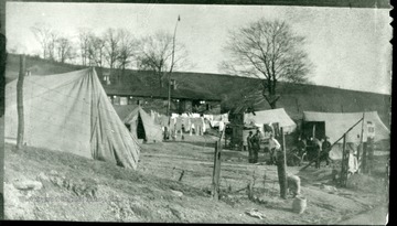 Tents and a laundry line are set up outside of a house. Men are standing talking outside of one of the tents.