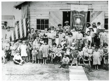 Group portrait of coal miners and their families sitting outside a barrack at Owings, West Virginia coal mining town.