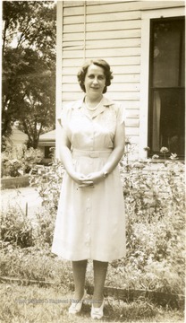 Portrait of Katherine Estenline, Director of Scott's Run Methodist Settlement House 1939-1941 standing outside a building near a flower garden.