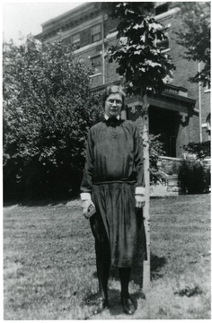 Portrait of Frances Kruger, Director of Scott's Run Settlement House 1929-1933 standing beside tree and in front of large brick building.