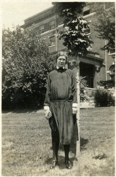 Portrait of Frances Krurger, Director of Scott's Run Settlement House 1929-1933 standing beside tree in front of large brick building. 
