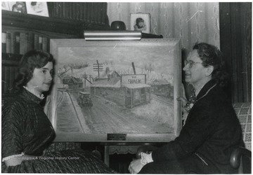 Artist Margaret Anne Christopher(left) and her Mother Mary sit in front of a painting of the Shack.