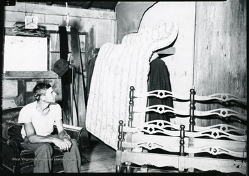 Man sits in a chair next to mattress, bed frame, and other items at the Scott's Run Reciprocal Economy Salvage building.