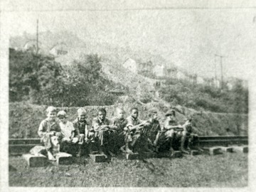 A group of children sitting on railroad tracks, with homes in the background.  'For more information on Mountaineer Mining Mission, see A&amp;M 2491 (S.C.)'