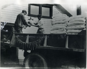 Two men move sacks of flour from the bed of a truck. 'For more information on Mountaineer Mining Mission, see A&amp;M 2491 (S.C.)'
