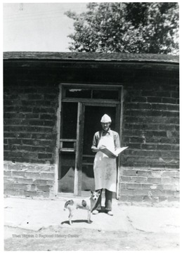Baker wearing white apron and hat with dog at his feet.
