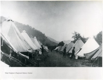 Soldiers stand between rows of tents. Troops Commanded by Gen. Bandholtz.