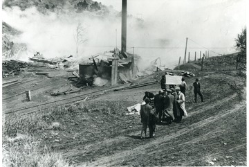 Smoldering remains of a building are in the background.