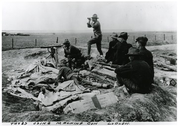 Men using a machine gun and sitting in surrounding area with guns.