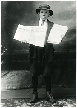 Young boy holding two copies of the newspaper The Miner's Herald.  Headline reads: 'Miners! Do Not be deceived.  Terrible strike is in Colorado.'