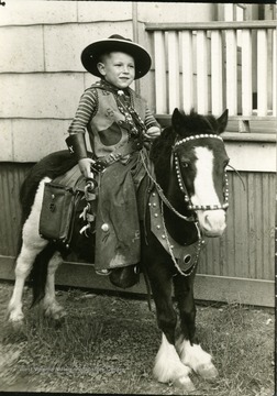 Edward Ozanic Jr. dressed in cowboy wear sitting on a small horse.