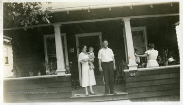 Women holding child, man, and others standing on porch of house 709. 