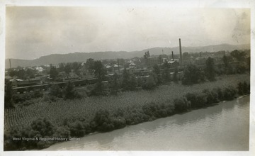 Large group of train cars at an industrial area beside a river. Photograph from Joe Ozanic scrapbook.