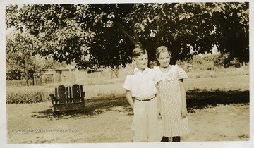 Boy and girl standing, the girl has her arm around the boy. 