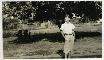 Boy standing alone with a tree in the background. 