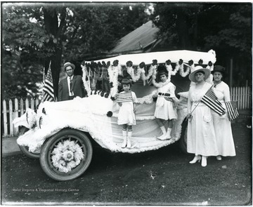 Man, two children, and two women stand near a car decorated for the Fourth of July parade.