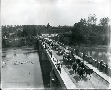 Fourth of July parade being led by a horse-drawn carriage on a bridge in Alderson, W. Va.  Banner reads '1776 Victory 1919'