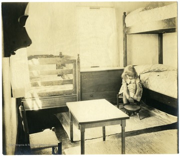 Child is tying her shoe next to a bunk bed in a the nursery of a homestead at Arthurdale.