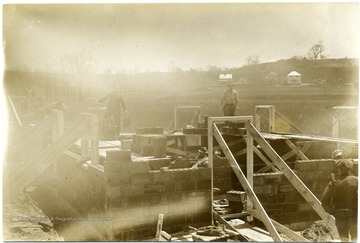 Men working on a half finished house. The window frames and door frames have been put in up to this point.