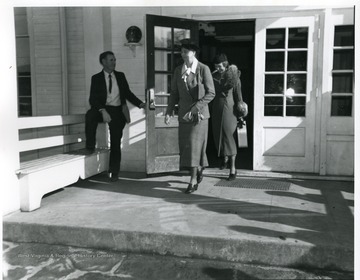 An unidentified gentleman is holding the door of the Community Center open for Mrs. Eleanor Roosevelt and an another woman.