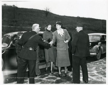 Mrs. Eleanor Roosevelt is shaking the hands with an unidentified man in uniform. Behind her are Jennings Randolph and Doris Duke.
