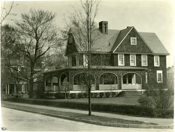 Three story house with archways on the porch and a side yard.