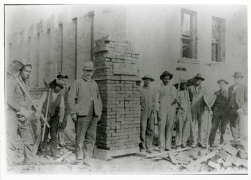 Construction crew workers stand around a pile of bricks.