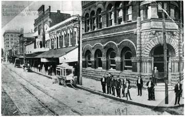Townspeople are standing in front of buildings located on Main Street, looking west, in Clarksburg, West Virginia.