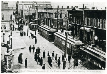 People on sidewalks next to trolley cars traveling in downtown Fairmont.