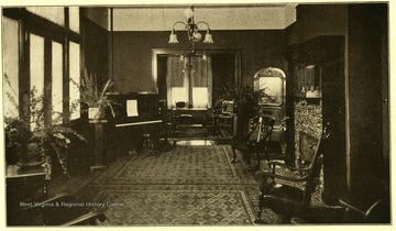 Parlor with rugs, chairs, a fireplace, and a piano in the corner.