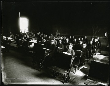 Students seated at their desks, teacher standing at the back of the classroom.