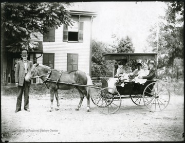 Family of four children and mother sitting in the carriage.  Man standing with the horse.