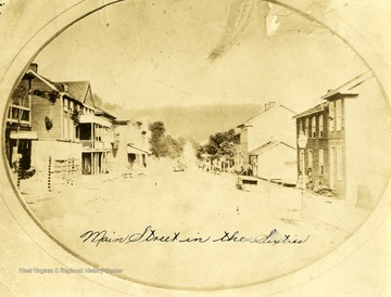 The back of a horse drawn wagon is seen moving down the dirt paved Main Street. 