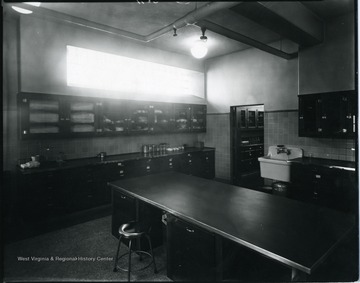 A table and a sink with cupboards on both walls.