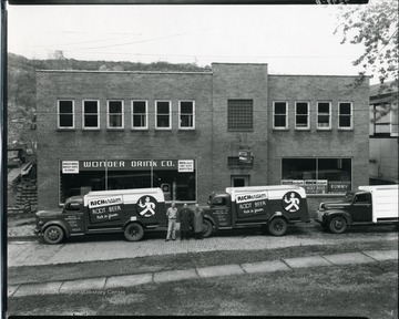 Three men are standing in front of two Richardson Root Beer trucks that are parked in front of the Wonder Drink Co., in Grafton, West Virginia.