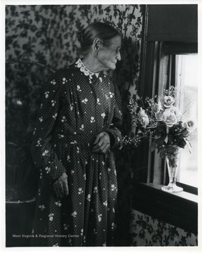 An old woman is standing by a window.
