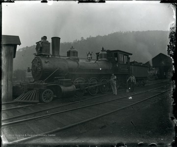 Two men stand next to Baltimore and Ohio Train Engine No. 578. One holds a shovel, the other is oiling the train.
