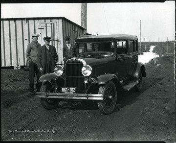 Three men standing beside a car on a dirt road, Grafton, W. Va.