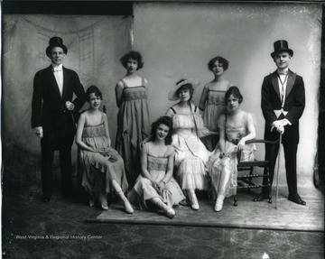 Two men are standing while five women are sitting.