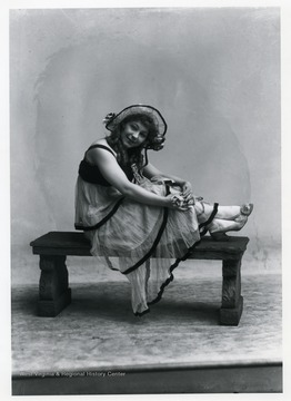 A woman wearing a dress and hat is sitting on a bench.