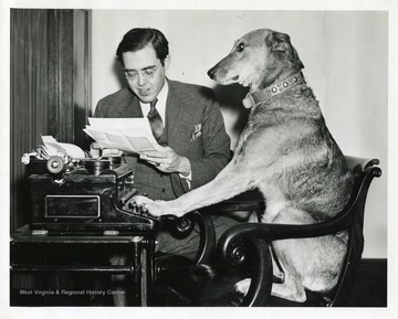 Senator Rush D. Holt is reading some papers while his dog is pretending to type.