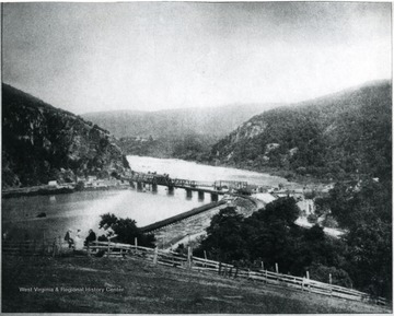Bridge at Harpers Ferry, W. Va.  'The most picturesque, beautiful, and historical spot in America.  The view is from the top of Bolivar Heights overlooking the city.  To the left is Md. Heights along the Potomac River, and to the right is Loudon Heights, in Va., along the Shenandoah River; the city itself being in W. Va.  The confluence of the two rivers takes place under the B.&amp; O. RR Bridge.  Harper's Ferry is generally conceded to be the birthplace of the Civil War.  A monument to John Brown has been erected alongside of the RR Track near the station.  The Old Government Arsenal, which was destroyed by the Confederates in 1861 was located along the Potomac at the foot of city.'  See Pamphlet number 7514 at the West Virginia and Regional History Collection for more information.