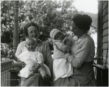 Olga Aegerter and another woman sitting on a porch swing while holding two babies.
