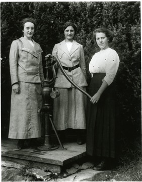 Olga Aegerter and two other women pose for a portrait next to a water pump in Helvetia.