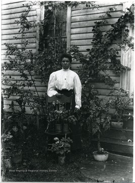Dora Huber, Helvetia's sole African American woman standing behind a chair with potted plants.