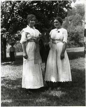 Two young women standing with a young horse in between them.  A young boy is standing in the background under a tree.  Helvetia, W. Va.