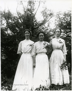 Three women standing together, small trees in the background, Helvetia, W. Va.