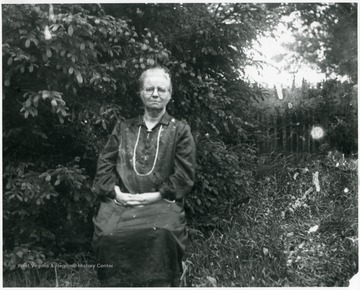 Older woman sitting in a fenced in brush area.  Helvetia, W. Va.